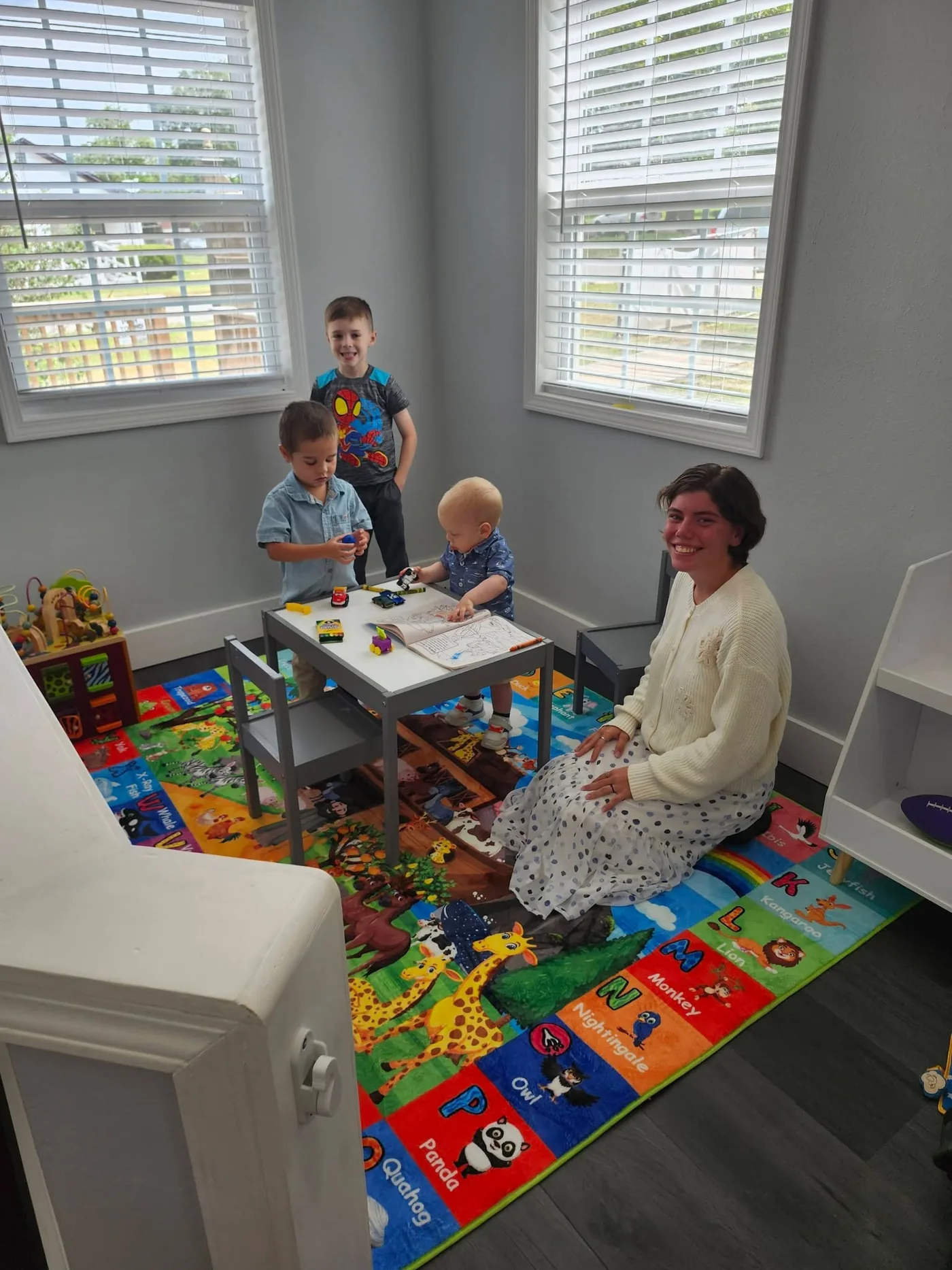 A mother and three young children at the little table in the Adkins Hall nursery, on the alphabet play mat