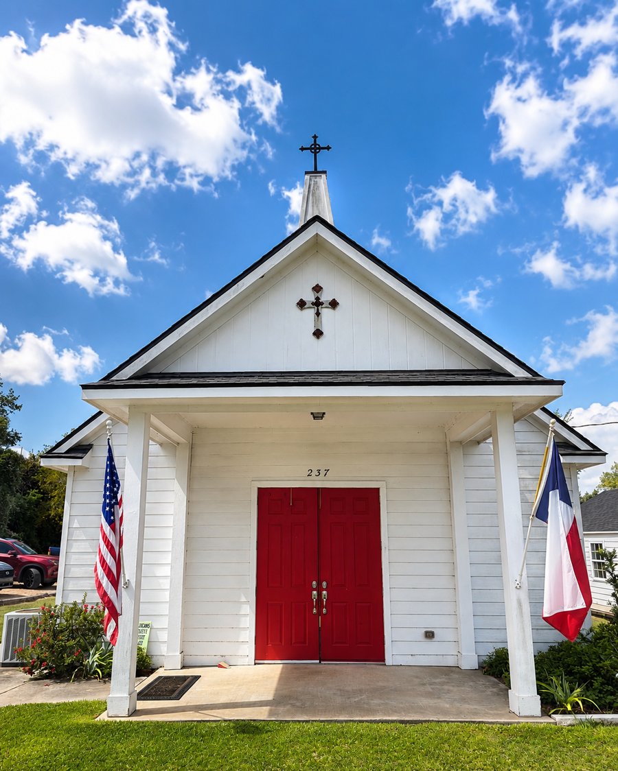 St. Barnabas Anglican Church, Bellville, Texas, exterior with red doors, cross, and American and Texas flags