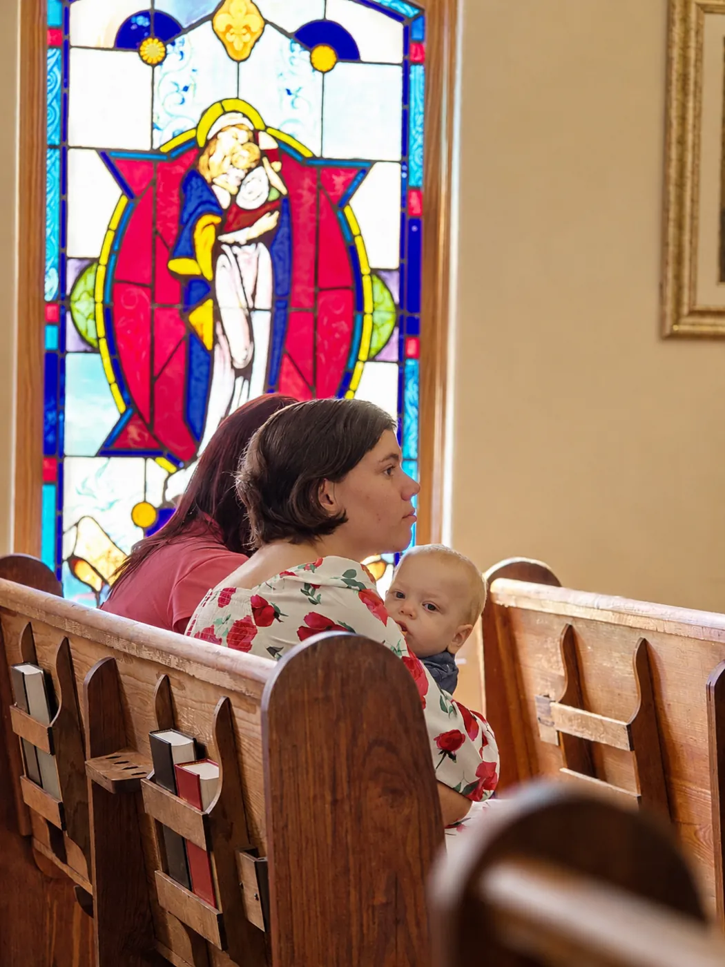 A mother holding her baby in the pew beneath the Madonna and Child window