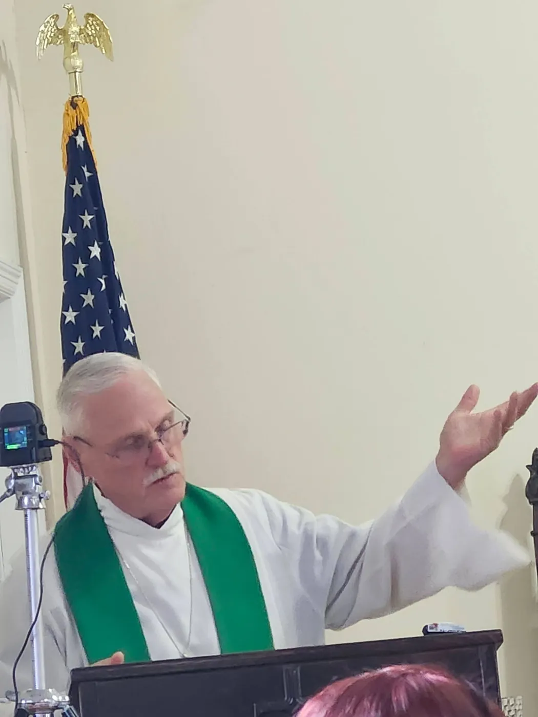 Fr. Mike Keppler preaching from the pulpit at St. Barnabas, arms open, in a green stole